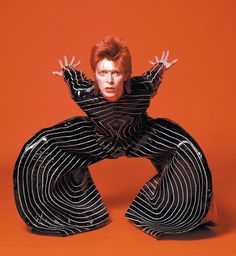 a man in black and white striped suit with his arms out, on an orange background