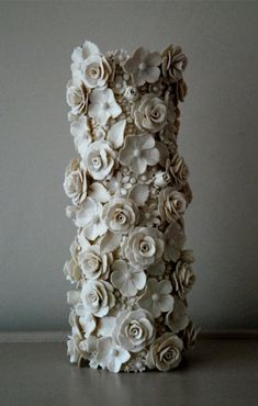 there is a tall vase made out of paper flowers on the table with white walls in the background