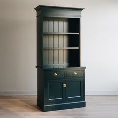 a dark green bookcase with brass handles and drawers on the bottom, in front of a white wall