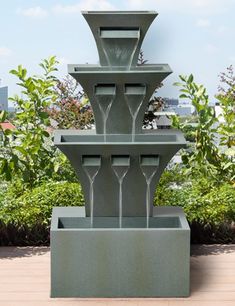 a tall fountain with three wine glasses on it's sides and trees in the background