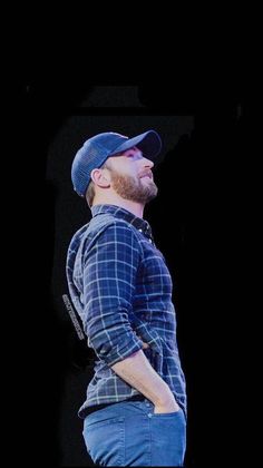 a man with a beard standing in front of a black background wearing a blue hat