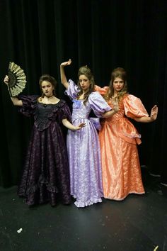 three women in dresses are posing for a photo on stage with an umbrella and fan