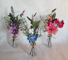 three glass vases with flowers and greenery in them