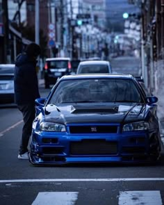 a blue car parked on the side of a road next to a person in a black jacket