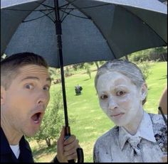 two people standing under an umbrella with white paint on their faces and one person holding an umbrella