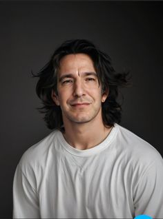 a man with long hair is smiling at the camera and wearing a white t - shirt