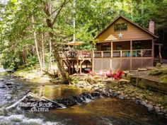 a cabin in the woods with a river running through it's foreground and trees surrounding