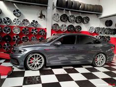 a grey car parked in front of a checkered black and white floor with tires on the wall