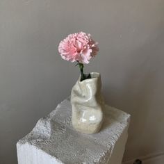 a white vase with a pink flower in it on top of a block of concrete