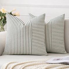 two green and white striped pillows sitting on a couch next to a vase with flowers