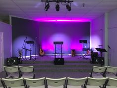 an empty stage with chairs and microphones in front of purple lights on the wall