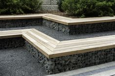 a wooden bench sitting on top of a gravel covered ground next to bushes and shrubbery