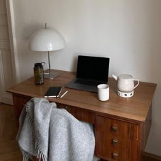 a laptop computer sitting on top of a wooden desk next to a lamp and cup