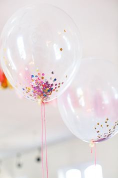 two clear balloons with confetti on them are in front of a white wall