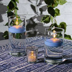 two lit candles sitting on top of a table next to glass vases filled with water