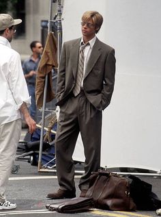 a man in a suit and tie standing next to another man on the street with luggage