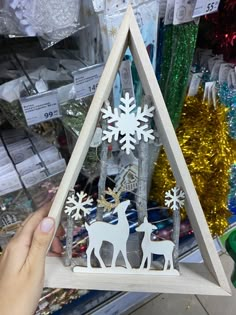 a hand is holding up a wooden triangle with deer and snowflakes on it