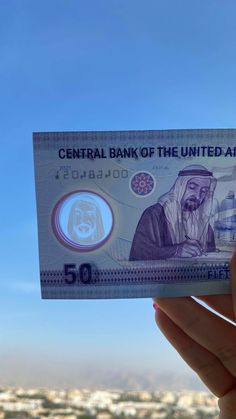 a person holding up a bank note in front of a cityscape and blue sky