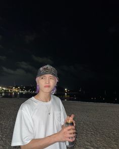 a young man standing on top of a sandy beach at night holding a drink in his hand