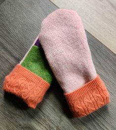 two pink and green mittens sitting on top of a wooden floor