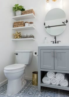 a white toilet sitting next to a bathroom sink under a mirror and shelves filled with towels