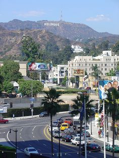 the hollywood sign is in the distance behind some palm trees and cars driving down the street