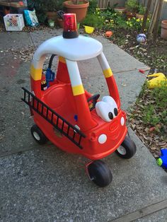 a little red firetruck is sitting on the sidewalk next to a toy truck