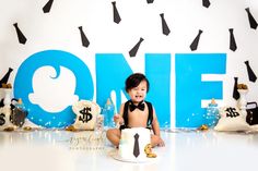 a little boy sitting on the floor in front of a one year cake with black and white decorations