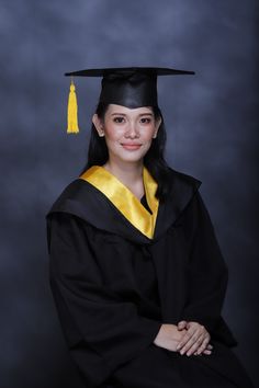 a woman wearing a graduation cap and gown posing for a photo in front of a dark background