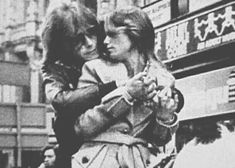 black and white photograph of two women hugging each other in front of a store window