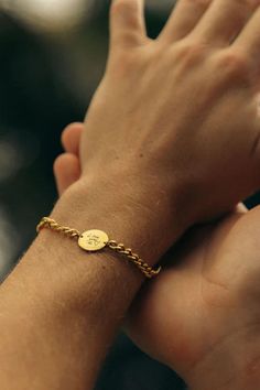 a person wearing a gold chain bracelet with a small disc on it's wrist