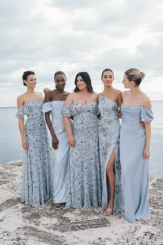 four women in blue dresses standing on the beach