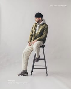 a man sitting on top of a stool wearing a jacket and hat with his legs crossed