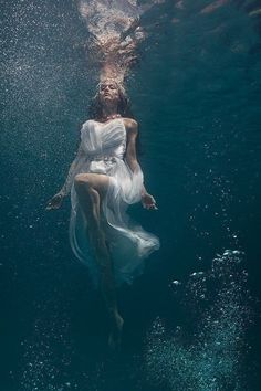 a woman floating in the water wearing a white dress