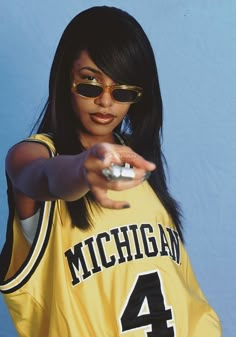 a woman in a yellow jersey holding a remote control and pointing at the camera with her right hand