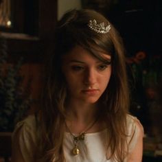 a young woman wearing a tiara and looking at the camera in a dimly lit room