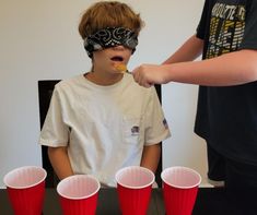 a young boy wearing blindfolds and eating food with red cups in front of him