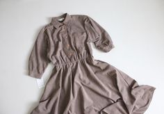 "Vintage 1980's taupe faux/ultra suede swing dress with button front, tab collar, stretch waist, and full flouncy skirt. Fits Like: Medium | No Label Size Circa 1980's Material: cotton-poly blend Condition: excellent Measurements: 38\" bust | 30-34\" waist | full hip | 17\" bodice length | 16\" shoulder | 44\" length" Faux Suede Dress, Suede Dress, Swing Dress, Faux Suede, Dress Clothes For Women, Bodice, Dress Outfits, Womens Dresses, Clothes For Women