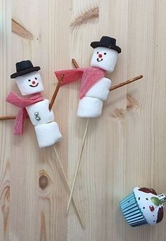 two snowmen made out of marshmallows on top of a wooden table