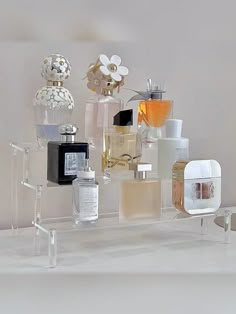 an assortment of perfumes are displayed on a clear display shelf in front of a white wall