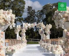 an outdoor wedding setup with white and pink flowers on the aisle, surrounded by wooden benches