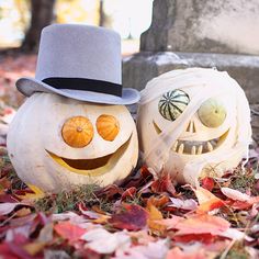 two pumpkins with faces painted on them sitting in leaves