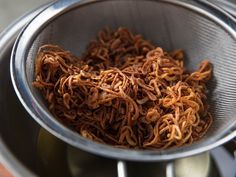 a strainer filled with brown noodles on top of a table