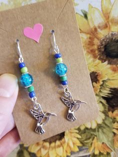 a pair of earrings with blue beads and charms on top of a piece of paper