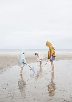 three people are standing on the beach and one is holding a net while another person holds a shovel