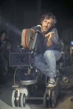 a man sitting on top of a camera in front of a projector with his hand pointing at the camera