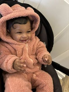 a baby sitting in a stroller wearing a pink bunny suit and smiling at the camera