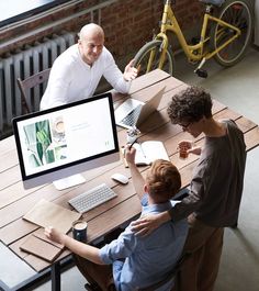 three people sitting at a table looking at a computer screen with an image on it