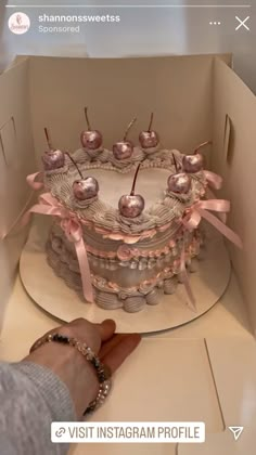 a person is decorating a cake with pink bows and cherries on it in a box