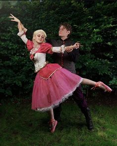 a man and woman dressed up in costume dancing on the grass with trees behind them